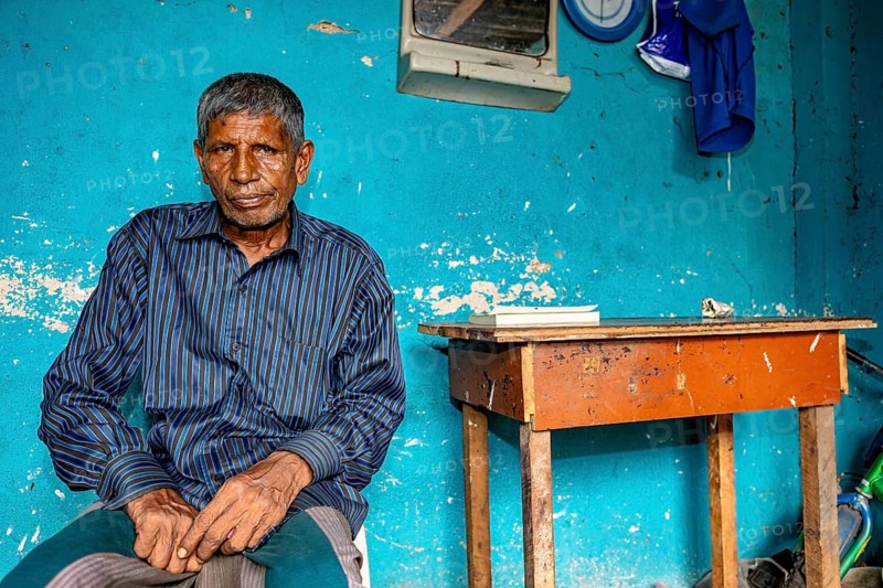 Man sitting relaxed in front of a blue wall in a simple room, people in the streets of Slave Island in Colombo Sri Lanka