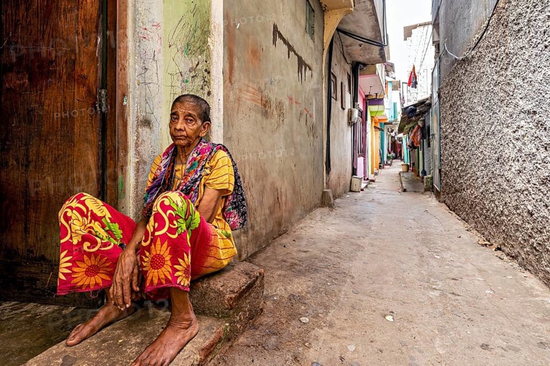 Elderly woman sitting pensively in a narrow alley, people in the streets of Slave Island in Colombo Sri Lanka