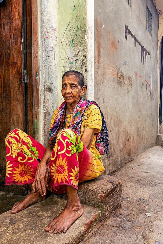 Woman in colorful clothes sitting on a step in a narrow street, people in the streets of Slave Island in Colombo Sri Lanka