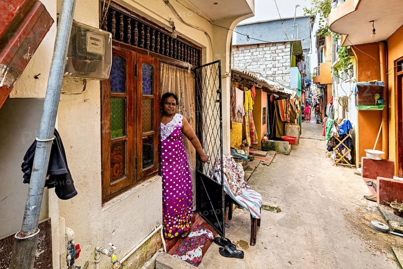Woman in traditional dress standing in front of a house in the alley, people in the streets of Slave Island in Colombo Sri Lanka
