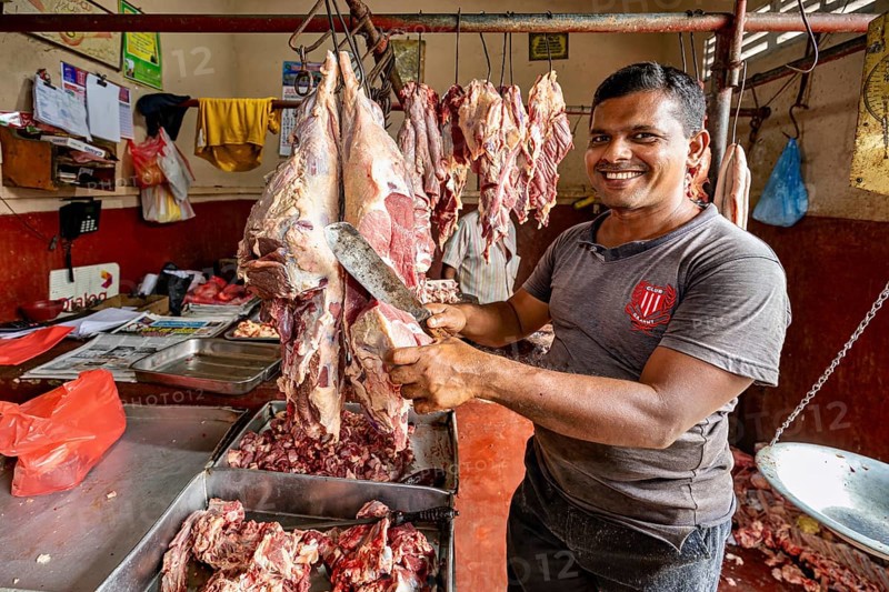 A smiling butcher cuts meat in a traditional shop, with pieces of meat around him, butcher shop in the streets of Slave Island in Colombo Sri Lanka