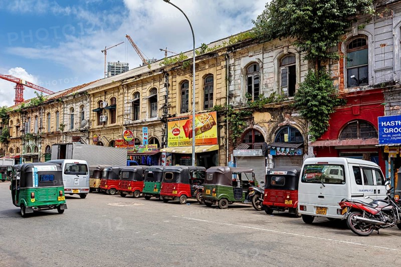 Busy urban street with old buildings and a series of tuk-tuks including a cloudy sky, tuk tuk in the streets of Colombo Sri Lanka