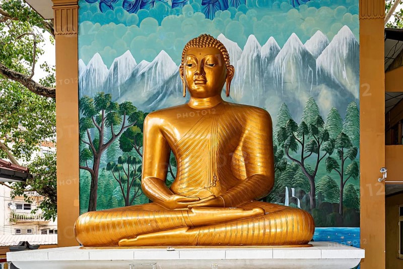 Golden Buddha statue in front of a painted wall with landscape motif, The Seema Malaka temple with the Buddha statues in Colombo Sri Lanka
