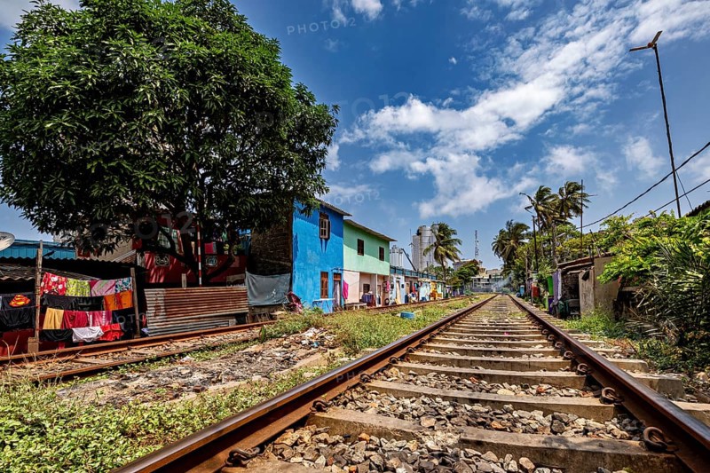 Railway tracks run along colorful houses and a large tree under a cloudy sky, railway line in the historic Slave Island district in Colombo Sri Lanka