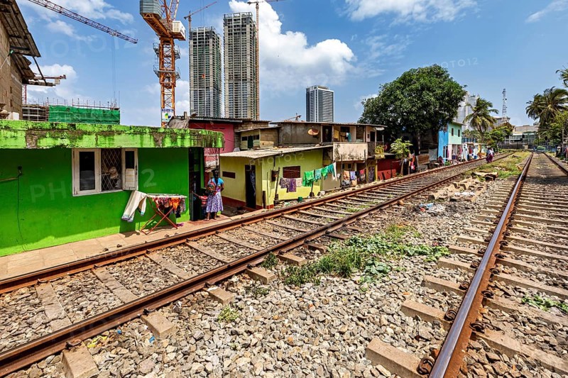 Railway tracks next to colorful houses with skyscrapers in the background and construction crane under a blue sky, railway line in the historic Slave Island district in Colombo Sri Lanka
