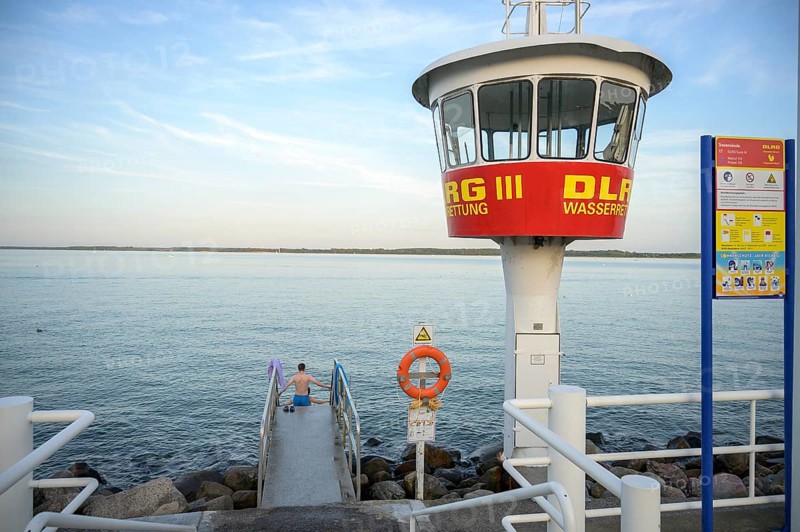 A modern DLRG watchtower looks out at the vast water while a bather sits on the jetty, Lübeck-Travemünde, Schleswig-Holstein, Germany