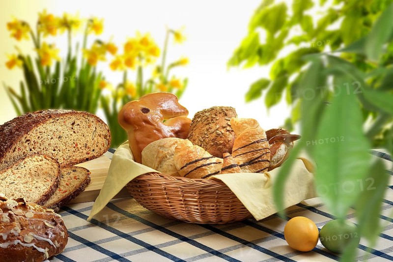 Easter basket with pastries, bread, Easter eggs, on checkered tablecloth, plants and flowers as decoration, studio shot