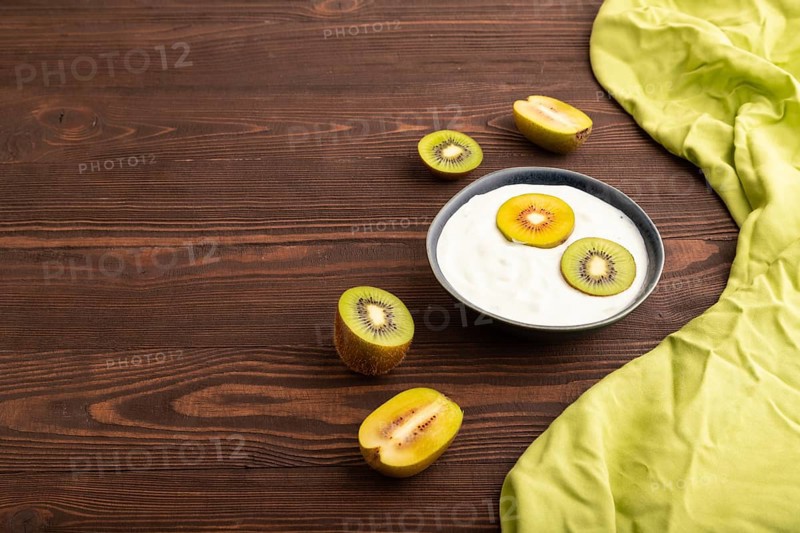 Yogurt, with kiwi in blue bowl on brown wooden background and green linen textile, side view, copy space, minimalism