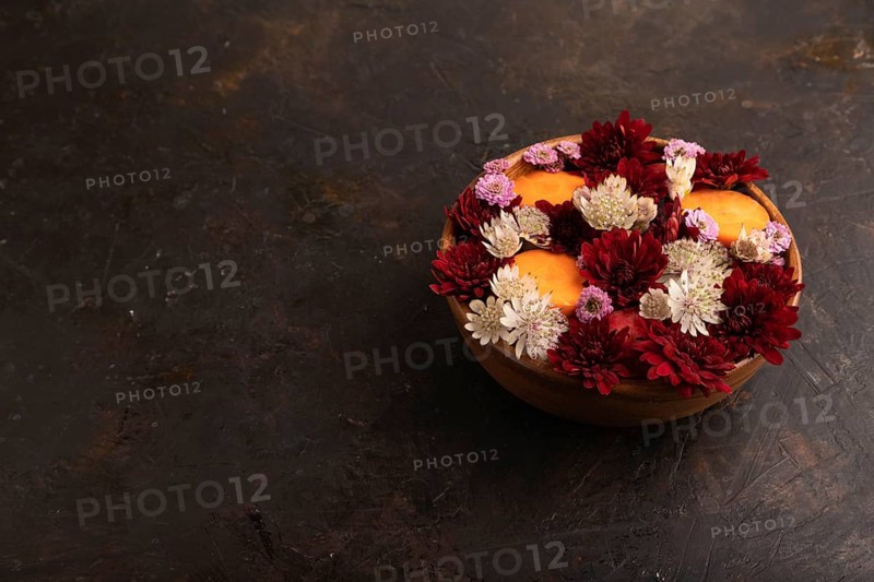 Wooden bowl with carrot slices and red Chrysanthemum flowers, Astrantia flowers, flower salad on black concrete background, side view, copy space, minimalism