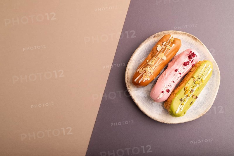 Glazed Eclairs on gray and brown pastel paper background, top view, flat lay, copy space