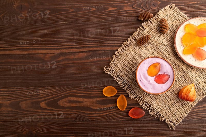 Purple Yogurt, with jelly candy on brown wooden background and linen textile, top view, flat lay, copy space, minimalism