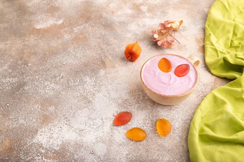 Purple Yogurt, with jelly candy on brown concrete background and green textile, side view, copy space, minimalism