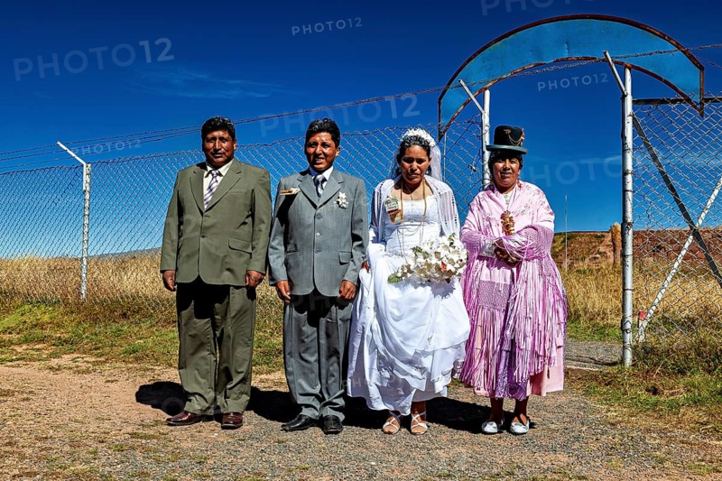 Wedding couple and companions in traditional clothes in front of fence and blue sky, traditional wedding in Bolivia