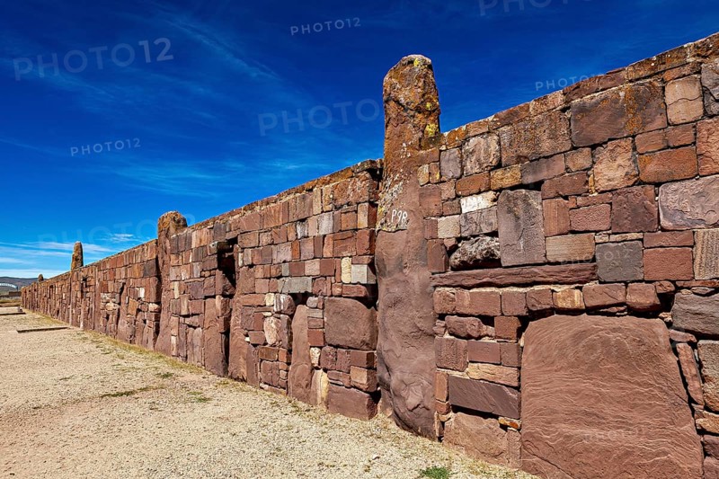Ancient stone wall stretching along a narrow path under blue sky, the archaeological site with the ruins of Tiwanaku in Bolivia