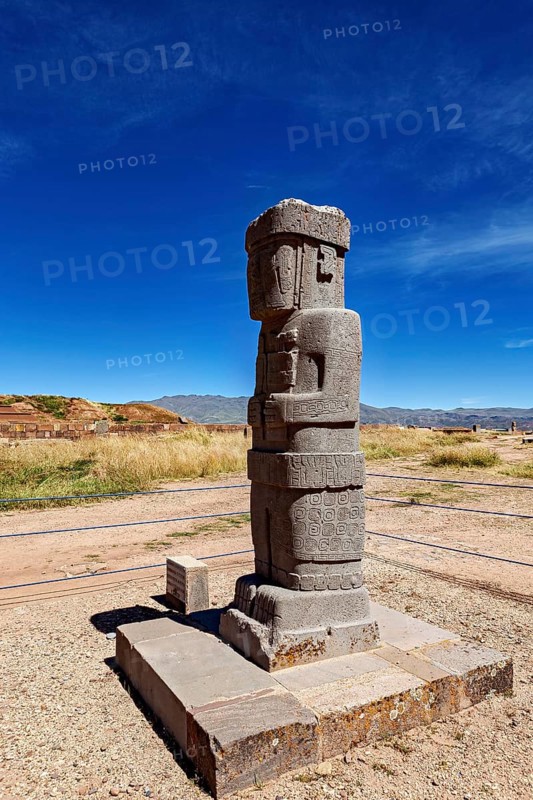 Ancient stone figure standing upright on a platform against a clear sky, the archaeological site with the ruins of Tiwanaku in Bolivia