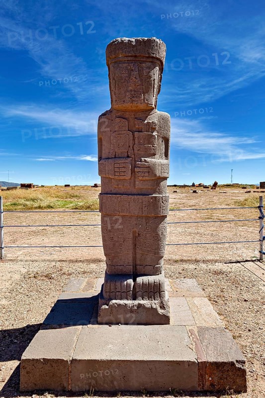 Ancient stone statue on a base in an open-air area under clear skies, The archaeological site with the ruins of Tiwanaku in Bolivia