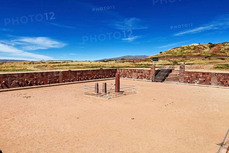 A rectangular square with stone pillars surrounded by ruins under a clear sky, The archaeological site with the ruins of Tiwanaku in Bolivia