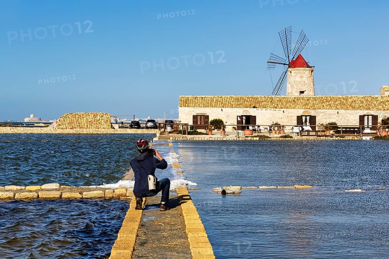 Cyclist photographs salt museum, traditional windmill, saltworks di Trapani and Paceco nature reserve, traditional salt production, Nubia, Trapani, salt route, Sicily, southern Italy, Italy