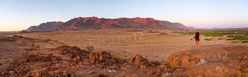 Young woman standing in desert landscape with Brandberg in morning light, at sunrise, Erongo, Damaraland, Namibia