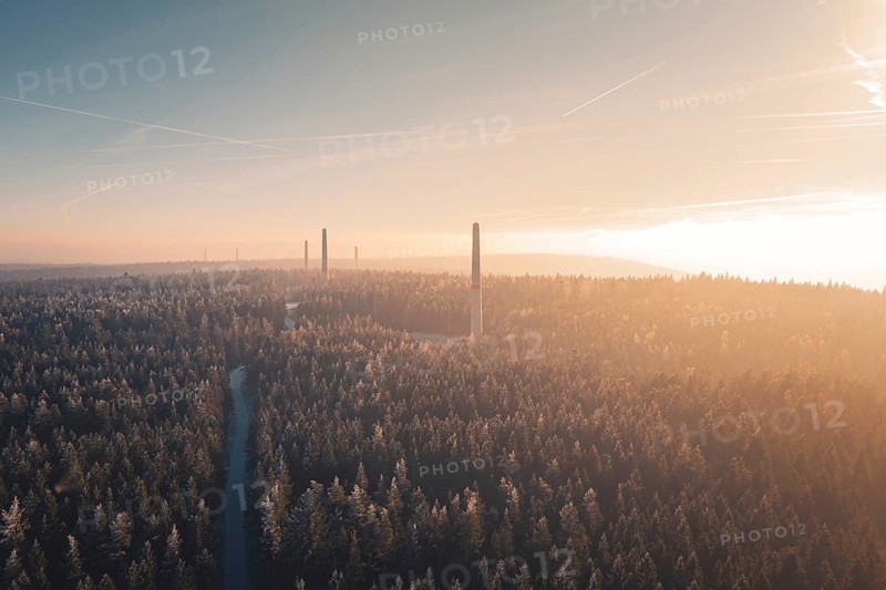 A dense forest with tall wind turbine towers on the horizon, surrounded by soft sunset light and fog, a wide and quiet atmosphere, Windkraft Bau, Besenfeld, Seewald, Freudenstadt district, Germany