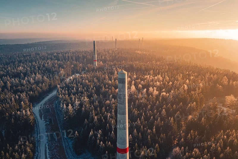 Narrow wind turbine towers rise above a snow-covered forest, winter silence and a curved path, in front of a bright evening sky, Windkraft Bau, Besenfeld, Seewald, Freudenstadt district, Germany