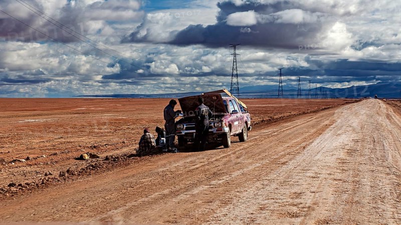A car is being repaired on the side of the road by several people in the desert, The landscape of the Altiplanos near Uyuni in Bolivia