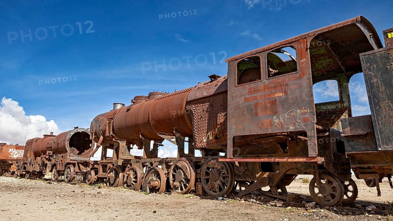 Long line of rusty locomotives in an open desert landscape under clear skies, old rusty locomotives at the train cemetery near Uyuni in the Altiplano in Bolivia