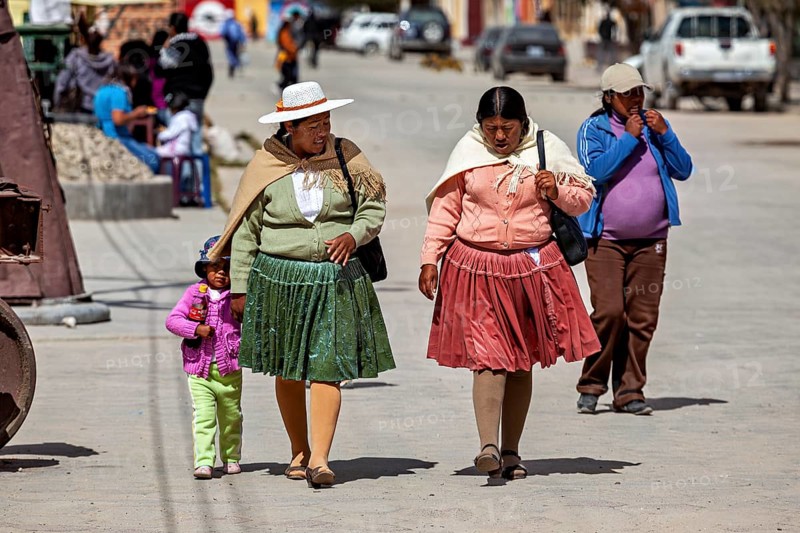 Two woman and a little girl walk down a busy street in traditional clothes, people in the altiplano near Uyuni in Bolivia