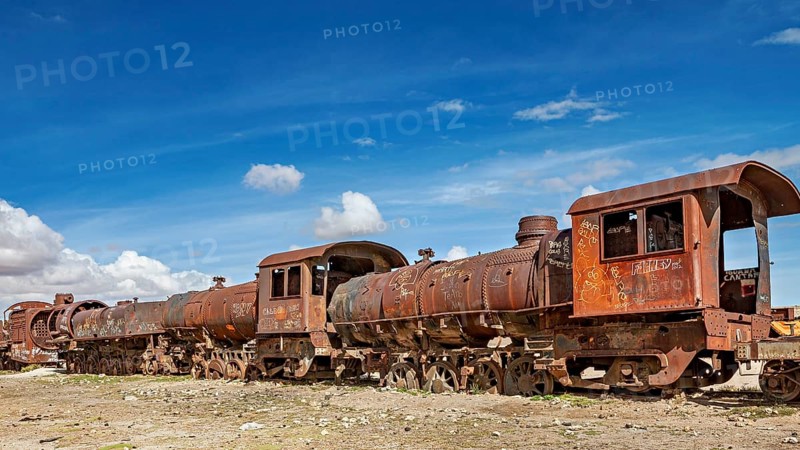 Rusty old trains on dry ground under blue skies, old rusty locomotives at the train cemetery near Uyuni in the Altiplano in Bolivia