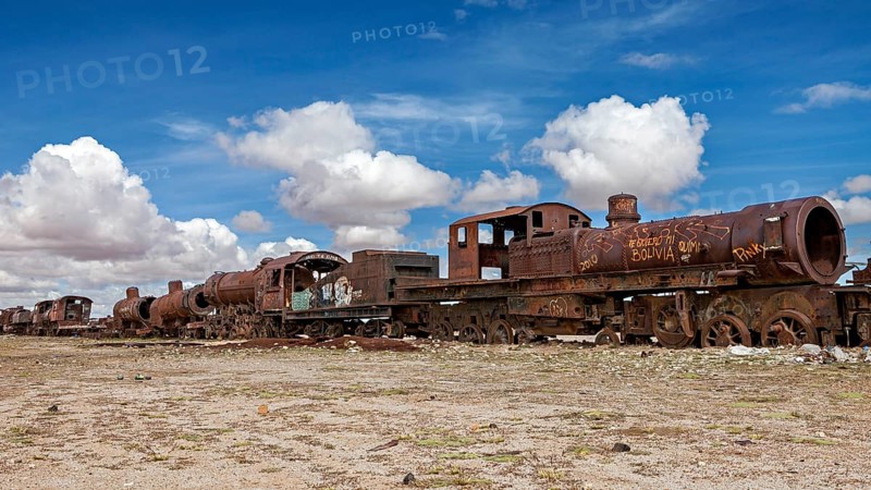 Abandoned and rusted locomotives under a clear sky with white clouds, old rusty locomotives at the train cemetery near Uyuni in the Altiplano in Bolivia