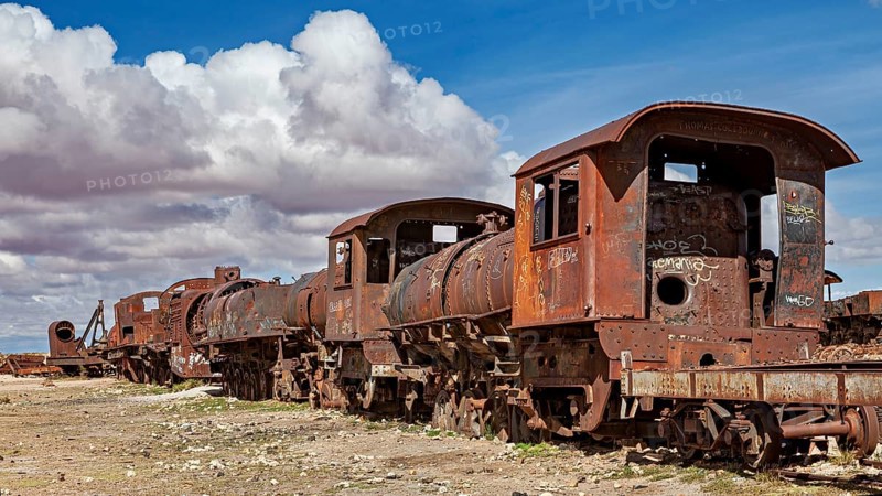 Several rusted locomotives on a dry surface under a cloudy sky, old rusty locomotives at the train cemetery near Uyuni in the Altiplano in Bolivia