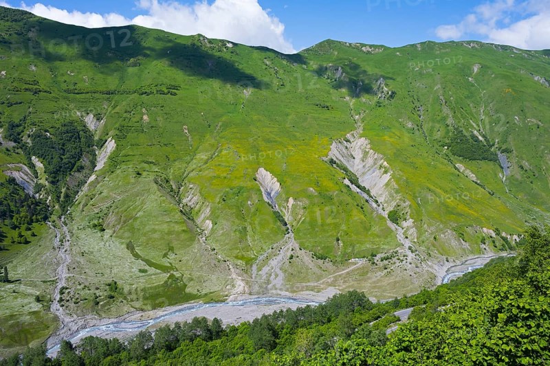 Green mountains and valleys with flowing river under blue sky, viewpoint near Gudauri, view of the mountainous landscape around Mleta, view of the White Aragvi River, Mtskheta-Mtianeti region, Georgian Military Highway, High Caucasus, Georgia