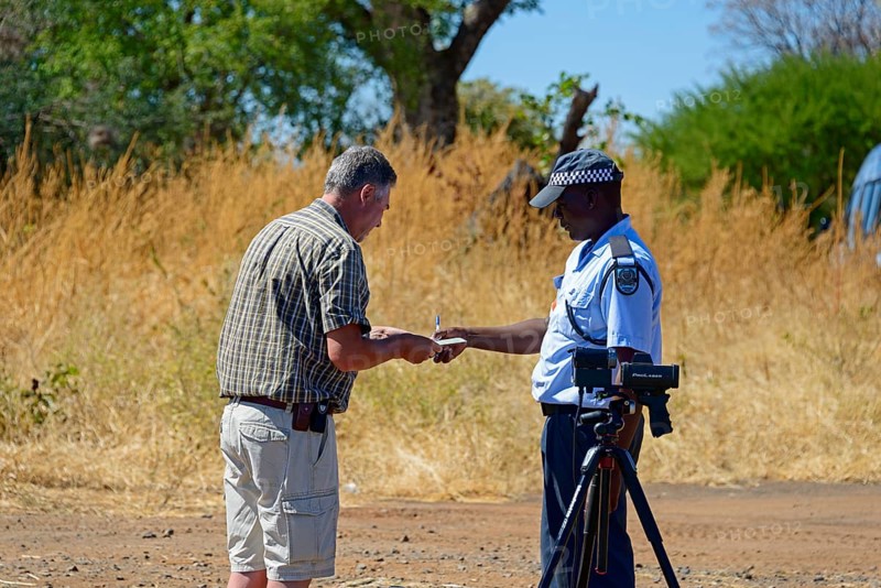 A police officer talks to a man on the side of the road in a rural setting, man must pay fine for driving at excessive speed, Botswana