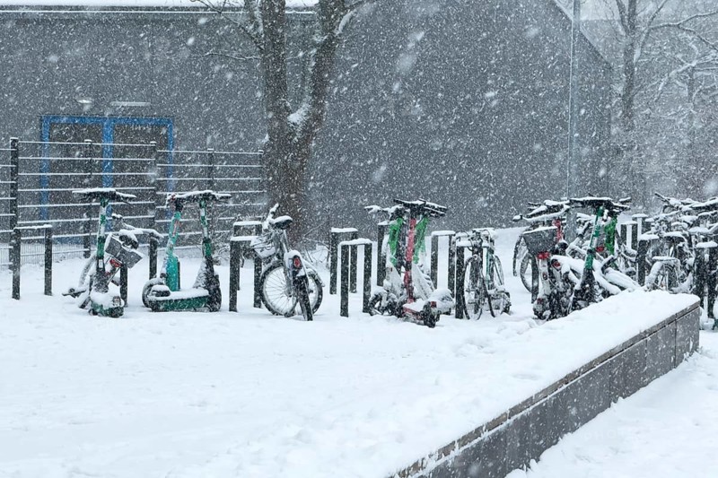 Tailored parked e-scooters and bicycles in winter during snowfall with snowflakes in the picture, Germany