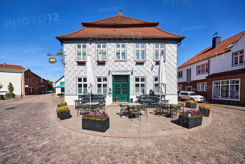 Alte Hofburg Imperial Palace pub, general architecture, commercial building, metal cladding, mansard roof, hipped roof, mansard hipped roof, red roof tiles, outdoor area of a restaurant with umbrellas, tables and benches, street made of paving stones, blue sky, cirrostratus clouds, Große Straße intersection with Rüschendorfer Straße, Damme, district of Vechta, Lower Saxony, Germany