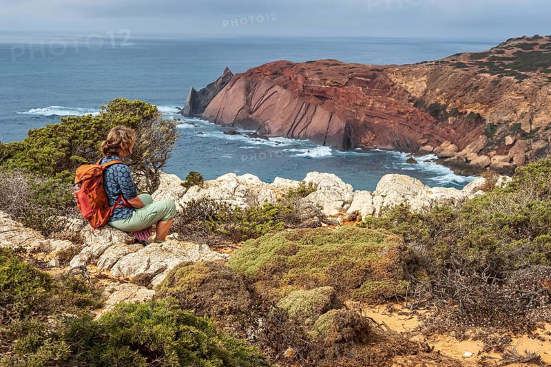 Hiking woman takes a break, view over cliff, Fishermens Trail, Rosa Vicentina, western Algarve just north of cape Cabo de Sao Vicente, Portugal