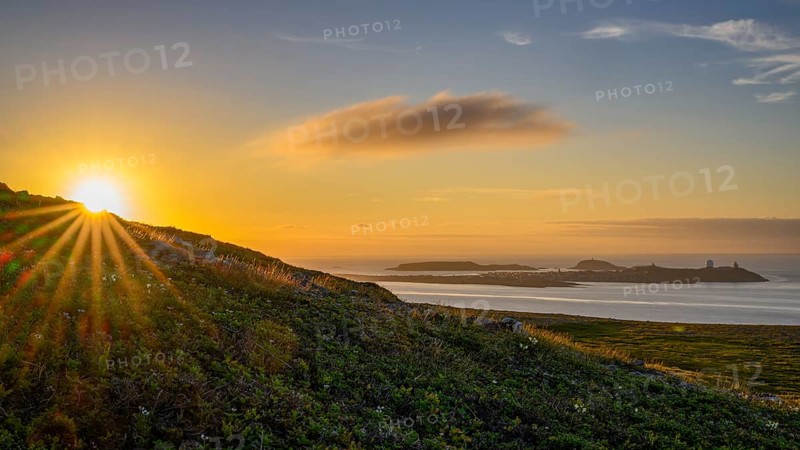 Midnight sun on Mount Domen in the background the city of Vardø, sea at sunset with golden sky and calm atmosphere, Kiberg, Finnmark, Norway