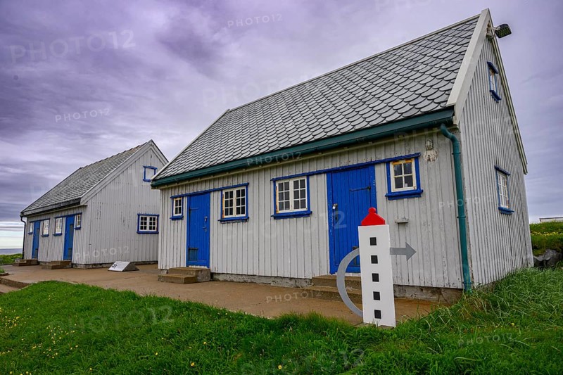 An old grey lighthouse dictionary house with a sloping roof at Kjølnes Fyr, small windows and railings in a rural area, Berlevåg, Finnmark, Norway