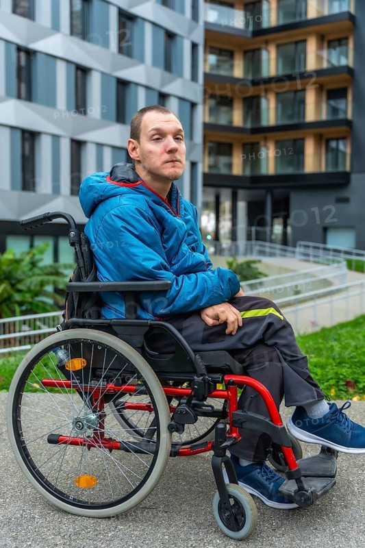Young adult man with a disability sitting in a wheelchair while looking forward, portraying concepts of mobility, independence, and inclusive urban lifestyle outside a modern building