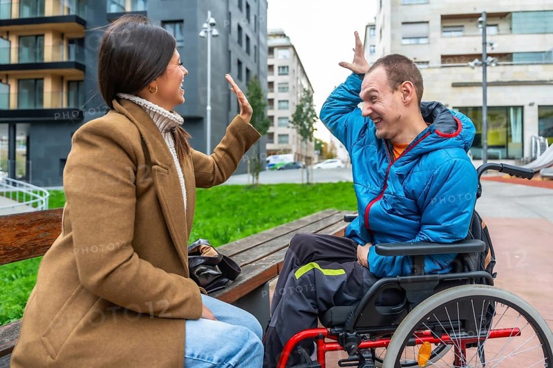Young woman on a bench in the city happily high fiving a smiling man in a wheelchair, illustrating friendship, support, and inclusion in an urban setting