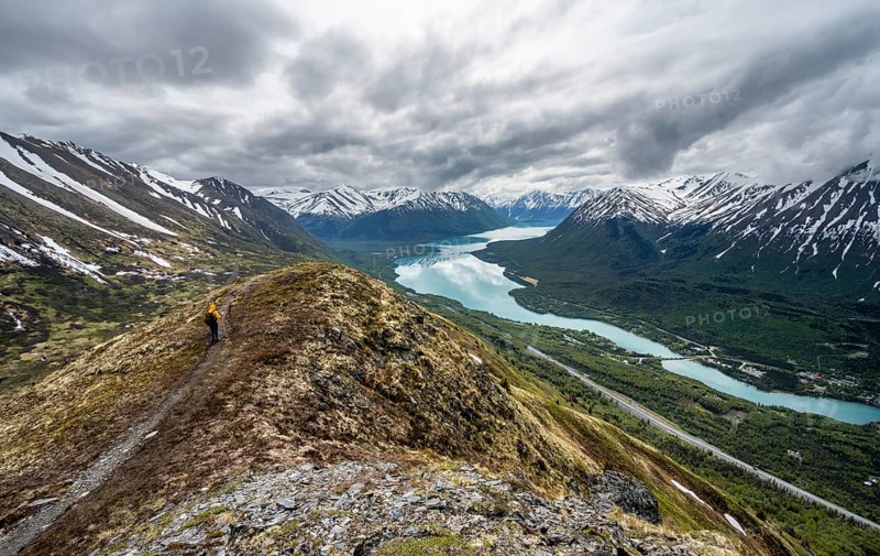Climbers on a hiking trail on Slaughter Ridge, views of snowy mountains in spring and turquoise Lake Kenai Lake, Cooper Landing, Kenai Peninsula, Alaska, USA