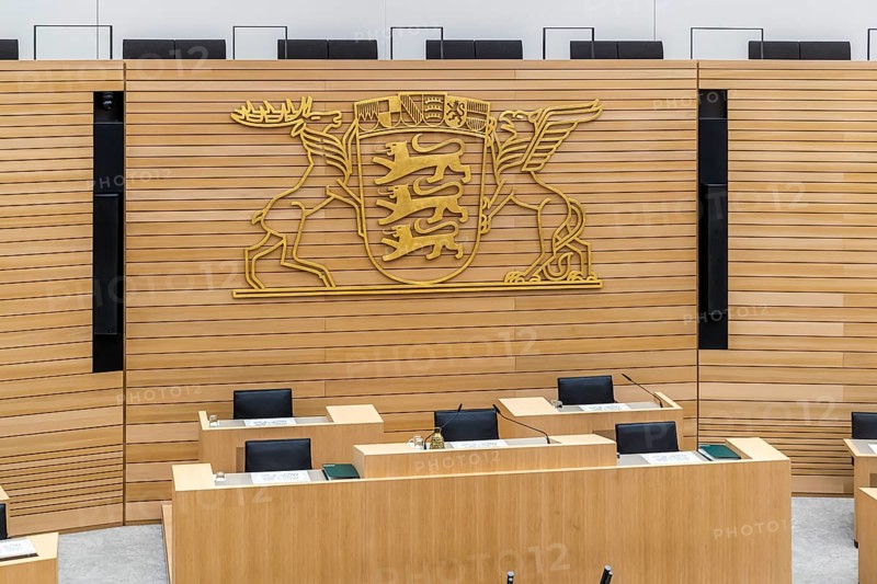 Plenary hall deserted with the seats of deputies and the government bank. Behind it is the coat of arms of the federal state. The state parliament of Baden-Württemberg is the state parliament based in Stuttgart, Baden-Württemberg, Germany