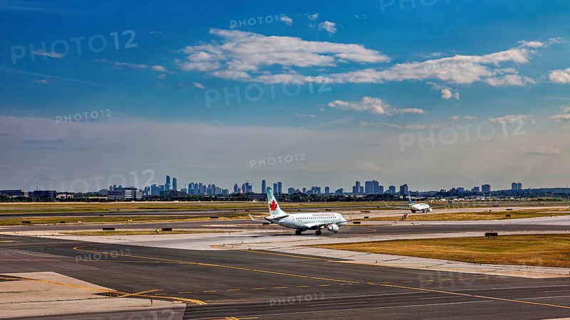 Airport with plane taking off in front of a skyline under a partly cloudy blue sky, view from an airplane of Toronto airport in Canada