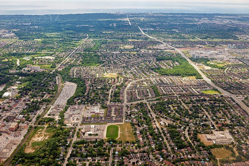 Densely populated residential areas and green spaces stretch out under a cloudy sky seen from the air, view from an airplane of the suburbs of Toronto in Canada