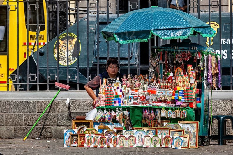 A woman sells colorful souvenirs at a street stand in a city with a bus in the background, a woman with her small street shop in downtown Lima in Peru
