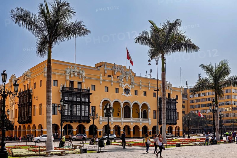 Colonial building with arches and national flag, surrounded by palm trees, in a sunny square, The historic center of Lima in Peru