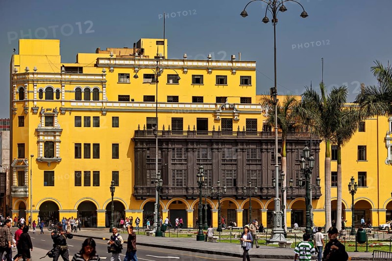 Yellow colonial building with wooden balcony on a busy street with strolling people, the historic center of Lima in Peru