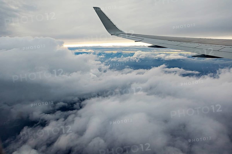 View of airplane wings above a thick cloud cover in the sky, In an airplane above the clouds