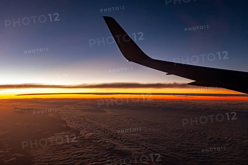 Airplane wings in front of a sunset over clouds, In an airplane above the clouds
