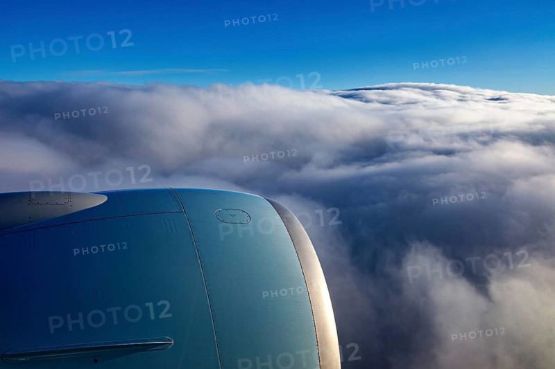 View from an airplane window of an engine and underlying clouds in the blue sky, on the plane above the clouds